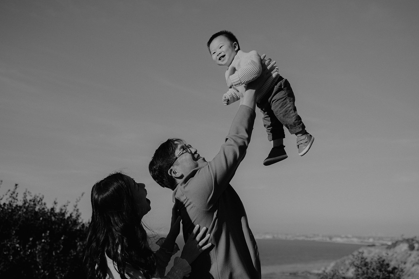 Father lifting his toddler into the air, dramatic black and white family portrait
