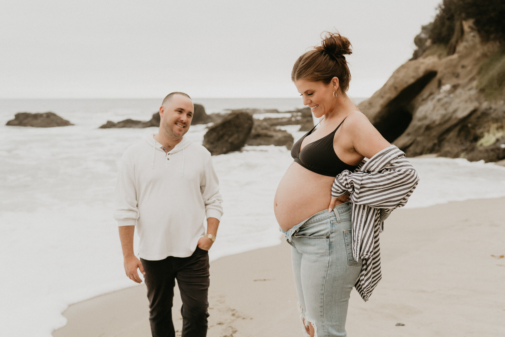 Couple sharing a moment as she lifts her shirt to reveal a pregnant belly on the beach