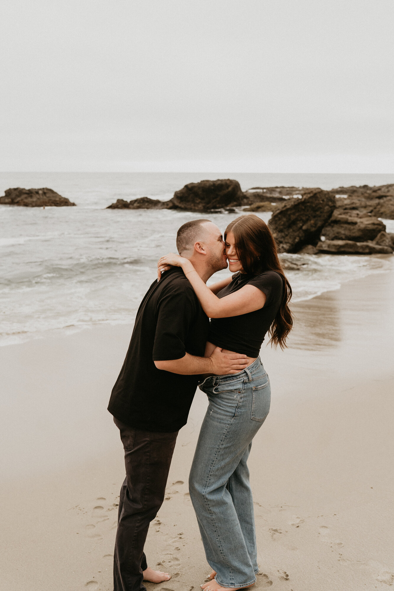 Pregnant woman in a black dress sitting in the sand, editorial maternity portrait